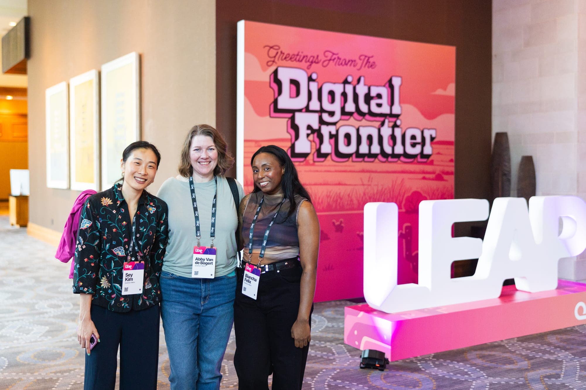 Three attendees posing in front of the Digital Frontier sign and LEAP letters